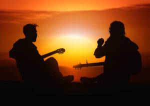two guitar players sitting in front of the sunset
