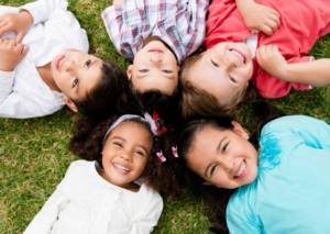 five kids leaying on the grass and smiling at the camera