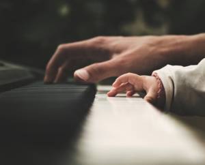 adult hand and child hand playing the piano